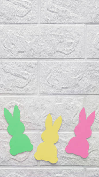 istock Three colored paper rabbits on white wall. Vertical photo. Place for text. 1980764642