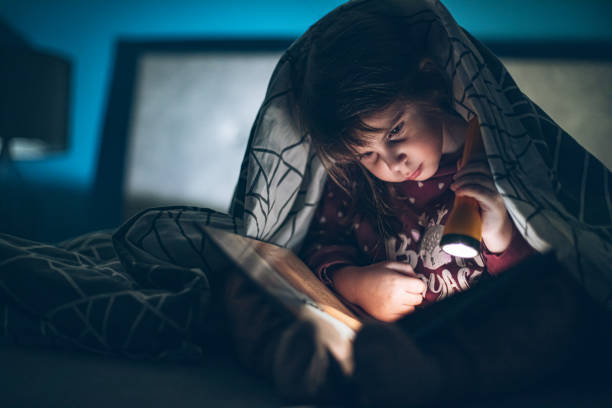 istock Little girl reading a book under a blanket in the dark 1980772017