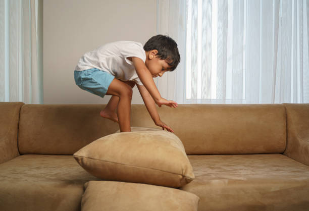 Cute little boy jumping and playing in a sofa at home