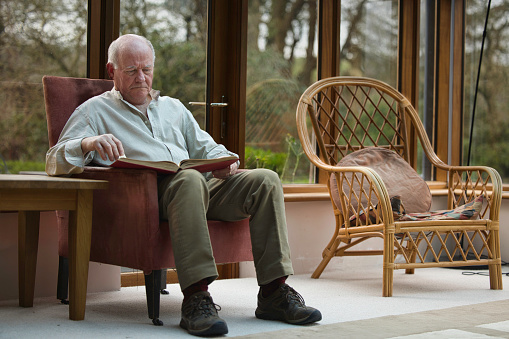 Senior man (60s) reading by stone fireplace.