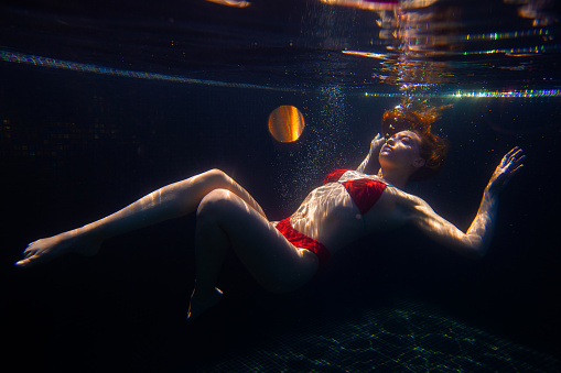 Girl in blue dress under water in the pool.