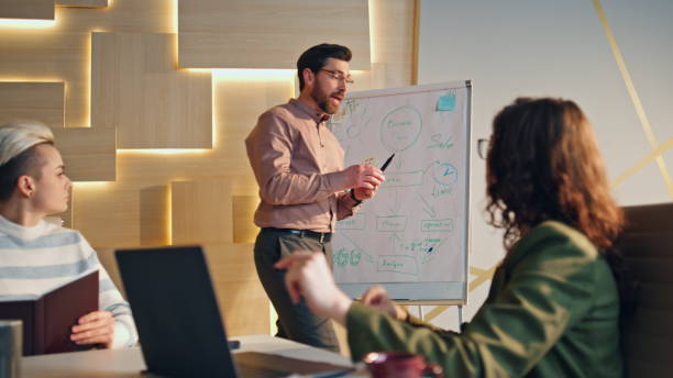 istock Business coach speaking audience in conference room. Young team clapping hands. 1980830440