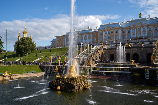 Saint Petersburg, Russia - June 09, 2023: Golden monuments with fountains and Grand Palace in Peterhof park near St. Petersburg. Built in 18th century laid out on the orders of Peter the Great. The palace-ensemble with fountains, gardens and monuments is recognized as a UNESCO World Heritage Site.