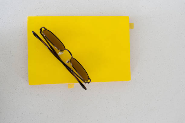 An overhead view of a vibrant yellow book paired with stylish dark sunglasses, arranged neatly on a light granite table