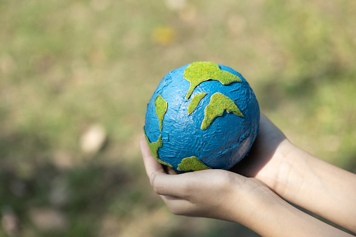 Young boy's hand holding planet Earth globe at natural park background as Earth day to save this planet with ESG principle and environment friendly energy for brighter future. Gyre