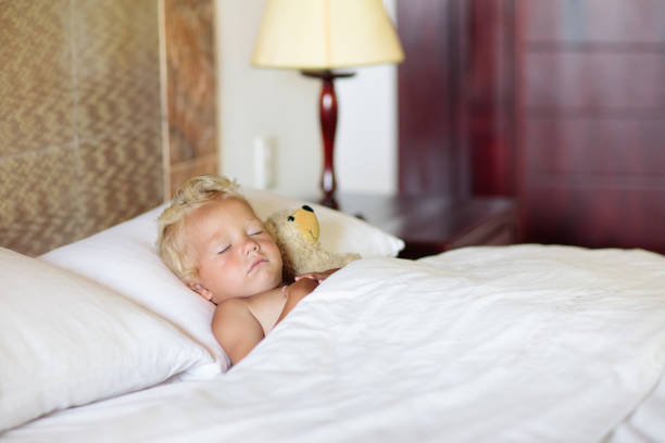 Baby sleeping in white bed. Healthy kids sleep. Little boy napping in parents bed. Sunny nursery for infant. Bedding for young child. Nap time. Toddler on sunny morning at home.