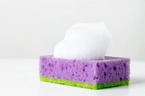Close-up of a wet sponge for washing dishes with soap sud. Space for copy.