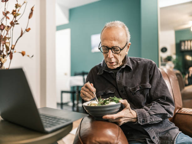 istock Senior man having a salad meal while using laptop in his living room 1980969012