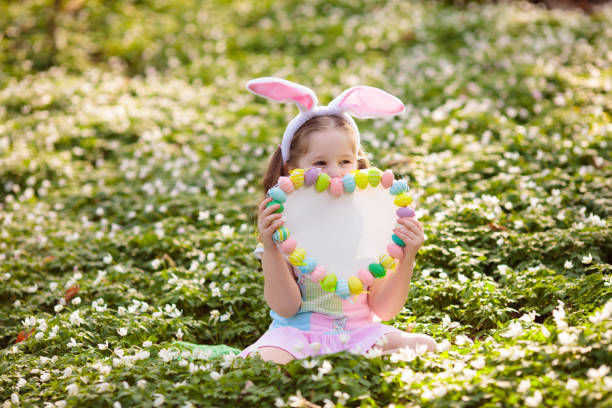 Child on Easter egg hunt in blooming cherry tree garden with spring flowers. Kid with colored eggs in basket. Little girl with bunny ears. Easter decoration, family celebration, Christian traditions.