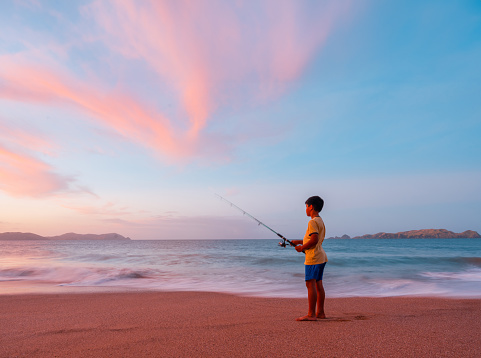 Kid enjoying fishing at beach at dusk in bay of islands, New Zealand.