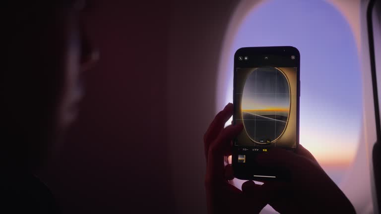 Female tourist taking photos from window of airplane with her mobile smart phone.