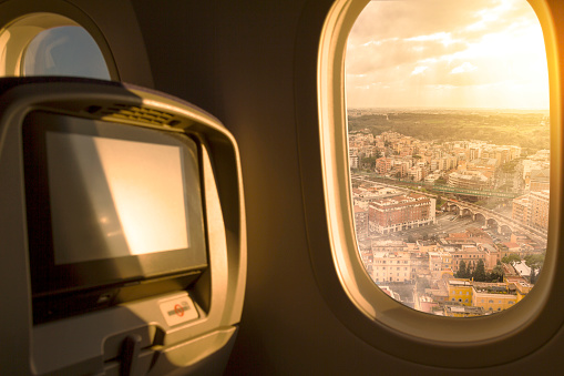 Rome City at sunset / sunrise sky aerial view from porthole window airplane economic seat after take off from airport. Travel concept. Plane interior.