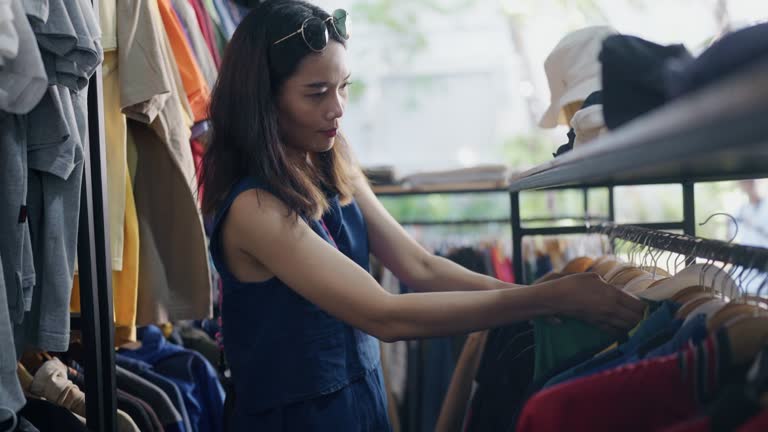 Asian woman tourist choosing T-shirt on rack in showroom in the 2nd hand market.