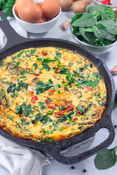istock Egg frittata with spinach, roasted red peppers, mushrooms, cheese and herbs, in cast iron, vertical 1981226661