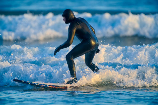 A surfer maneuvers skillfully on a wave off the coast of Mölle, Sweden. The vibrant sea and clear skies create an exhilarating atmosphere for surfing enthusiasts.
