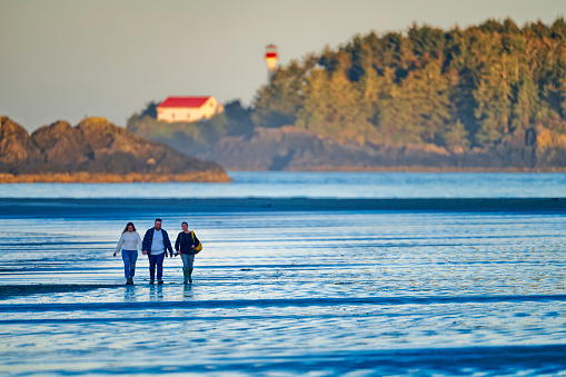 The Pacific Rim National Park on Vancouver Island on April  28, 2023:   Friends walking along the shoreline of Pacific Rim National Park on Vancouver Island at sunrise, British Columbia