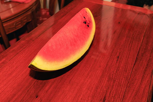 A quarter of a watermelon on a shiny rosewood table. It is ready to eat.