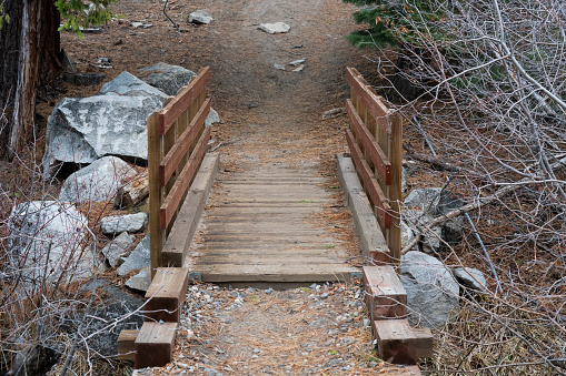 Wooden foot bridge on trail across small creek.  Granite rock on other side of path.  Winter.