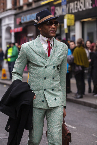 London, UK 02/21/2016 Smart cool style man wearing a mint green suit, shirt and tie and trilby fedora hat and sunglasses walking along a London street