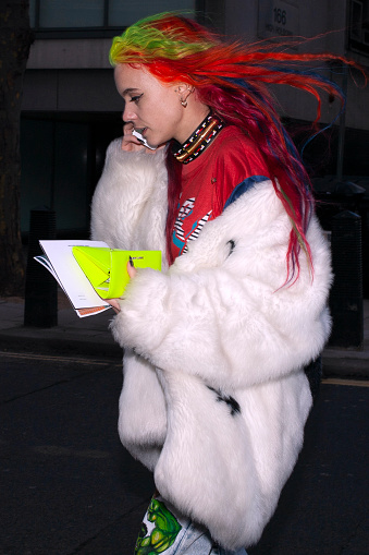 London, UK 01 09 2015 Chic woman in photo in profile view with  green hair dyed red hair wearing  a white faux fur coat and red top walking outdoors on a London street
