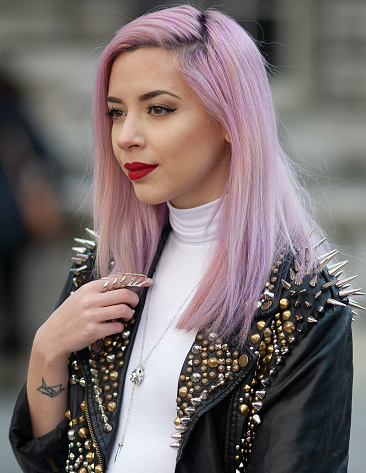 London, UK 02 21 2015 Photo of woman in profile with pink  hair, red lipstick, white polo neck turtle neck top and black studded jacket with spikes standing outdoors on a London street