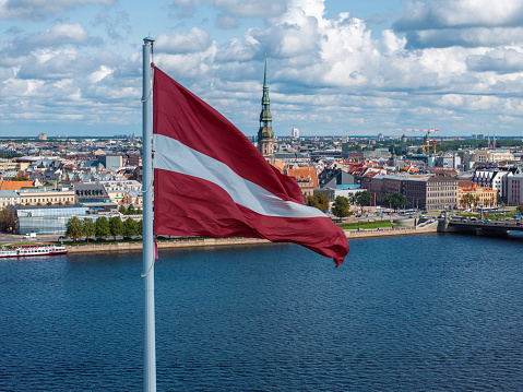Beautiful Latvian flag flutters on wind with Riga old town in the background in Latvia. Patriotic video. Panoramic view.