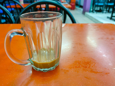 An empty teh tarik drink glass is on the table in a restaurant.