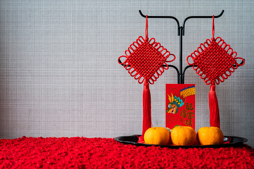 A red envelope or ang pao (words mean dragon and good luck) with hanging pendants and oranges on the tray for Chinese new year concept.