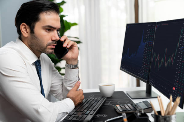 istock Trader calling to consultant or partner with two stock exchange screen. Surmise. 1981600713