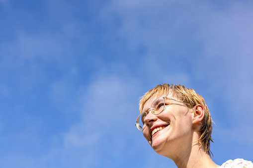 Portrait of happy young woman with eyeglasses, outdoor, low angle view, blue sky background with copy space, full frame horizontal composition