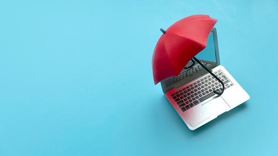 Computer and network security concept. Red umbrella cover the laptop over a blue background.