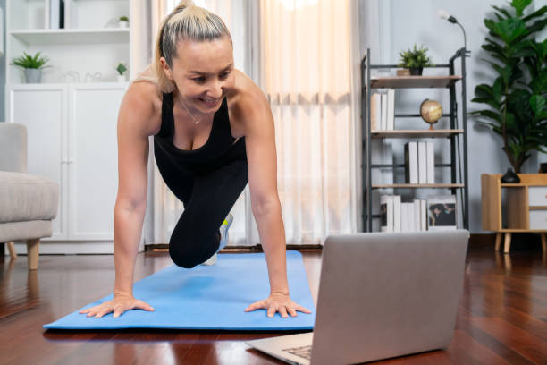 Athletic and active senior woman doing online plank climbing at home. Clout Athletic and active senior woman doing exercise on fit mat with plank climbing at home exercise while watching online exercising video as concept of healthy fit body lifestyle after retirement. Clout burpee stock pictures, royalty-free photos & images