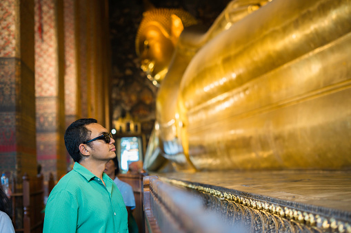 asian travel standing in front of Golden Reclining Buddha Statue at Wat Pho in Bangkok Thailand