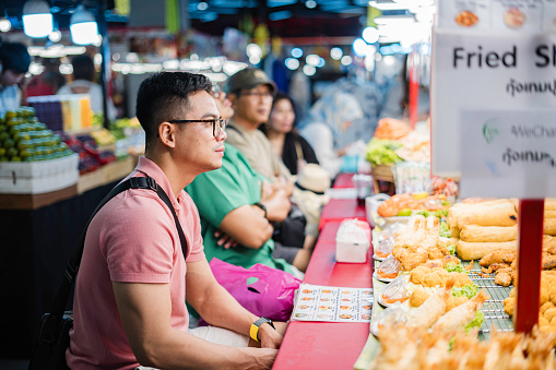 asian traveler tourist enjoy eating street food on the street at night market in Bangkok, Thailand. Holiday vacation trip.