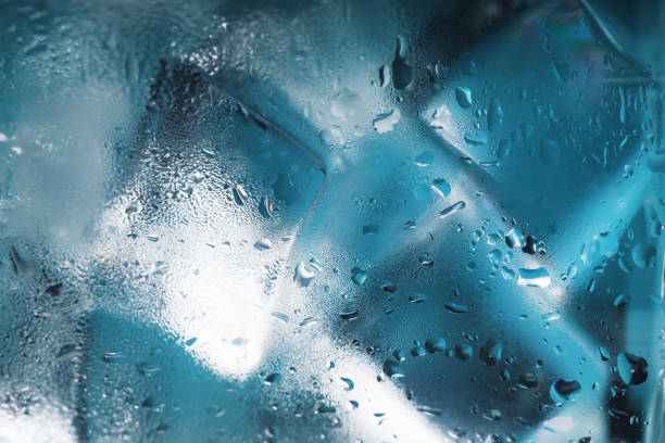 A glass with ice water and ice cubes on a blue background. A refreshing and chilling drink in hot weather.