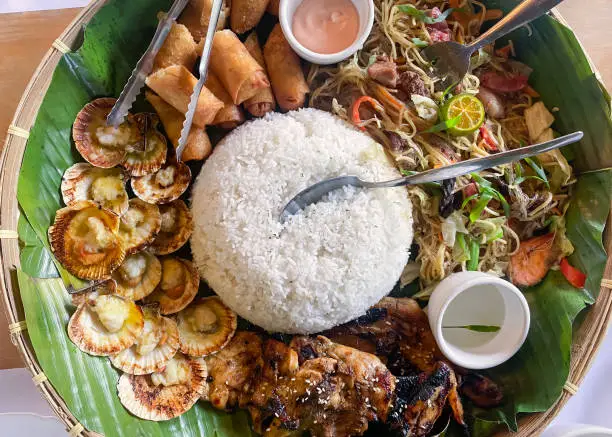 Filipino food on a plate with a banana leaf base. Rice, chicken, lumpia, pansit.