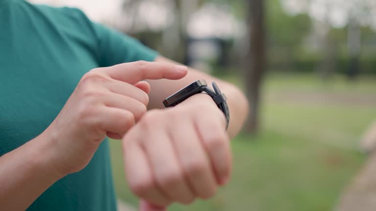 Close-up shot of woman touching and setting on smartwatch, using smart watch app, at public park.