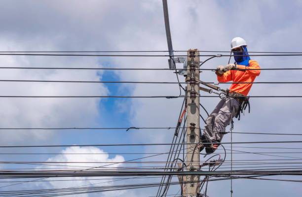 istock Electrician with work tools is installing cable lines and electrical system on electric power pole against blue sky background, 1982029945