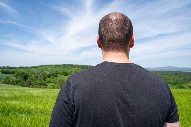 Guy stand in front of a grain field  and forest trees in the countryside in spring
