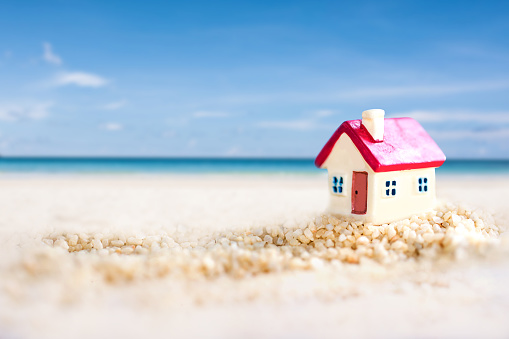 miniature house with red roof on tropical sand beach over blurred clear sky on day noon light.