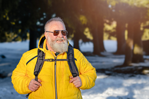 Portrait of a handsome senior backpacker with sunglasses in the snowy forest