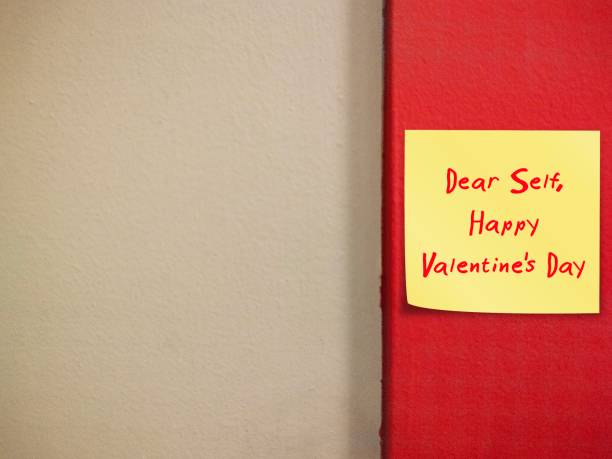 Note paper stick on red copy space wall with handwritten text DEAR SELF - HAPPY VALENTINE'S DAY - concept of self-love, single person give themselves love and care message on Valentine's
