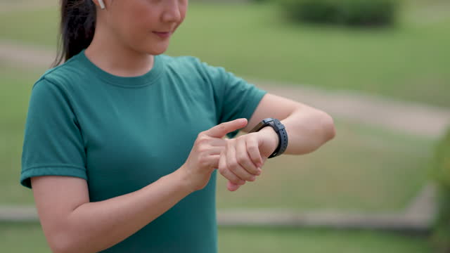 Close-up shot of woman touching and setting on smartwatch, using smart watch app, at public park.