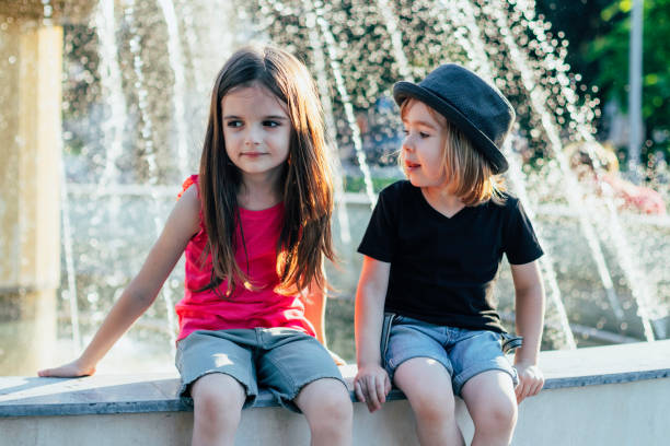 Two girls, sisters, smiling at the camera from a rock at the edge of an old granite quarry pond. Taken on an autumn day in Minnesota, USA.