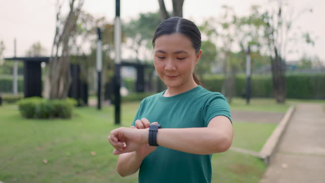 Asian woman looking and touching on smartwatch, using smart watch app, at public park.