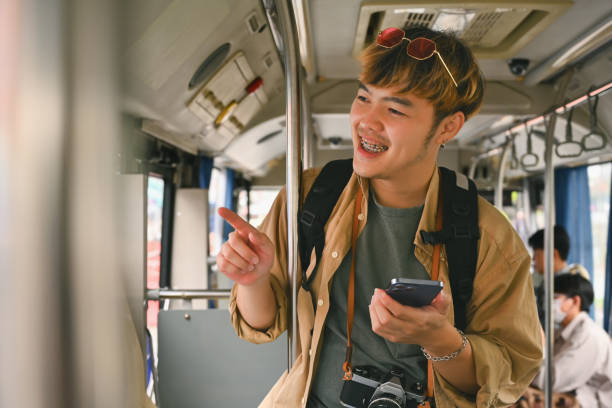 istock Smiling Asian man with backpack standing in bus and traveling with public transport 1982124022