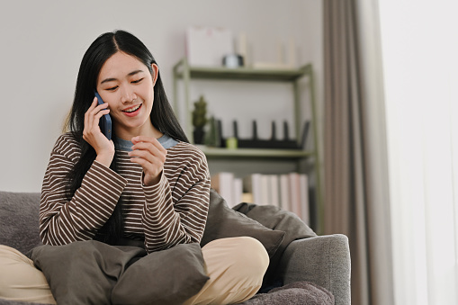 Beautiful young woman having phone conversation, sitting on couch at home.