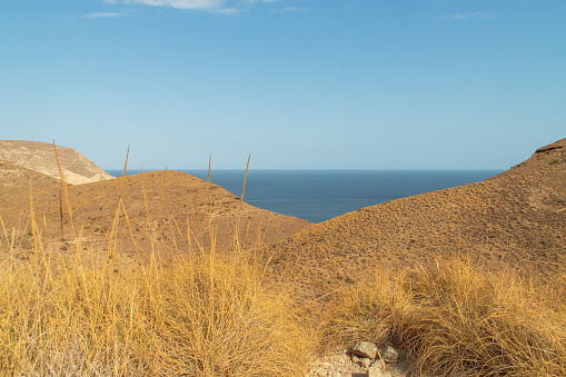 Steep rocky slopes covered with dry grass in summer next to the Mediterranean Sea. Cabo de Gata Natural Park.