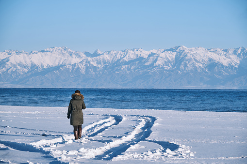 Female tourist is walking on Issyk-Kul lake shore on a cold sunny winter morning and streaming by wearable camera