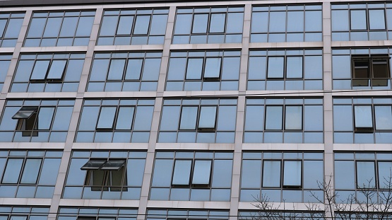 The facade of a modern building with many windows is an image in gray, urban architectural background, an office building with windows are ajar as a texture of the city without people